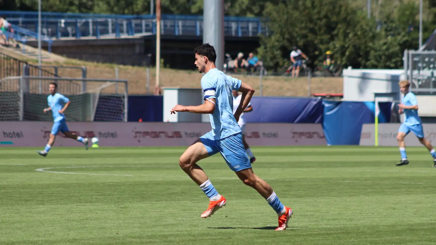Futbalista Šale v svetlomodrom drese vedie loptu stredom ihriska, okolo neho ďalší hráči